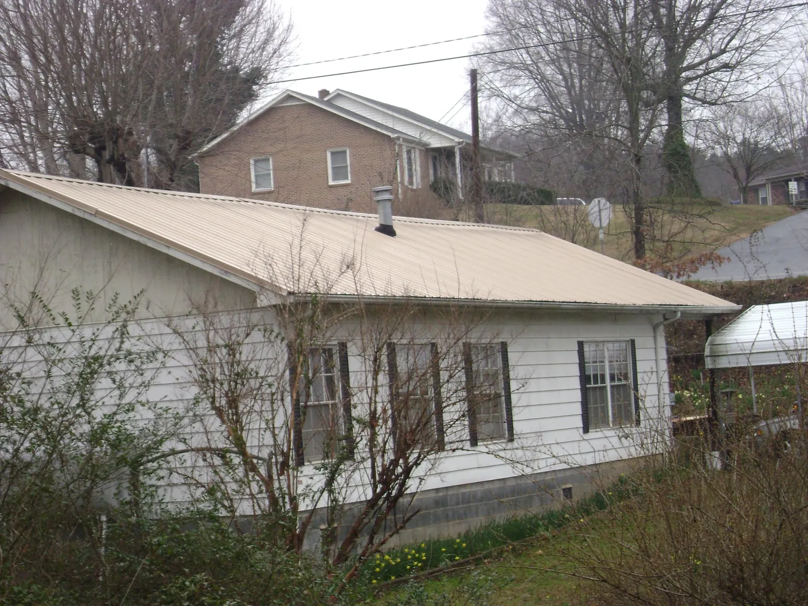 Tan metal roof on a white sided house set into a hillside — Commercial Roofing by Roofing Brothers in Pulaski